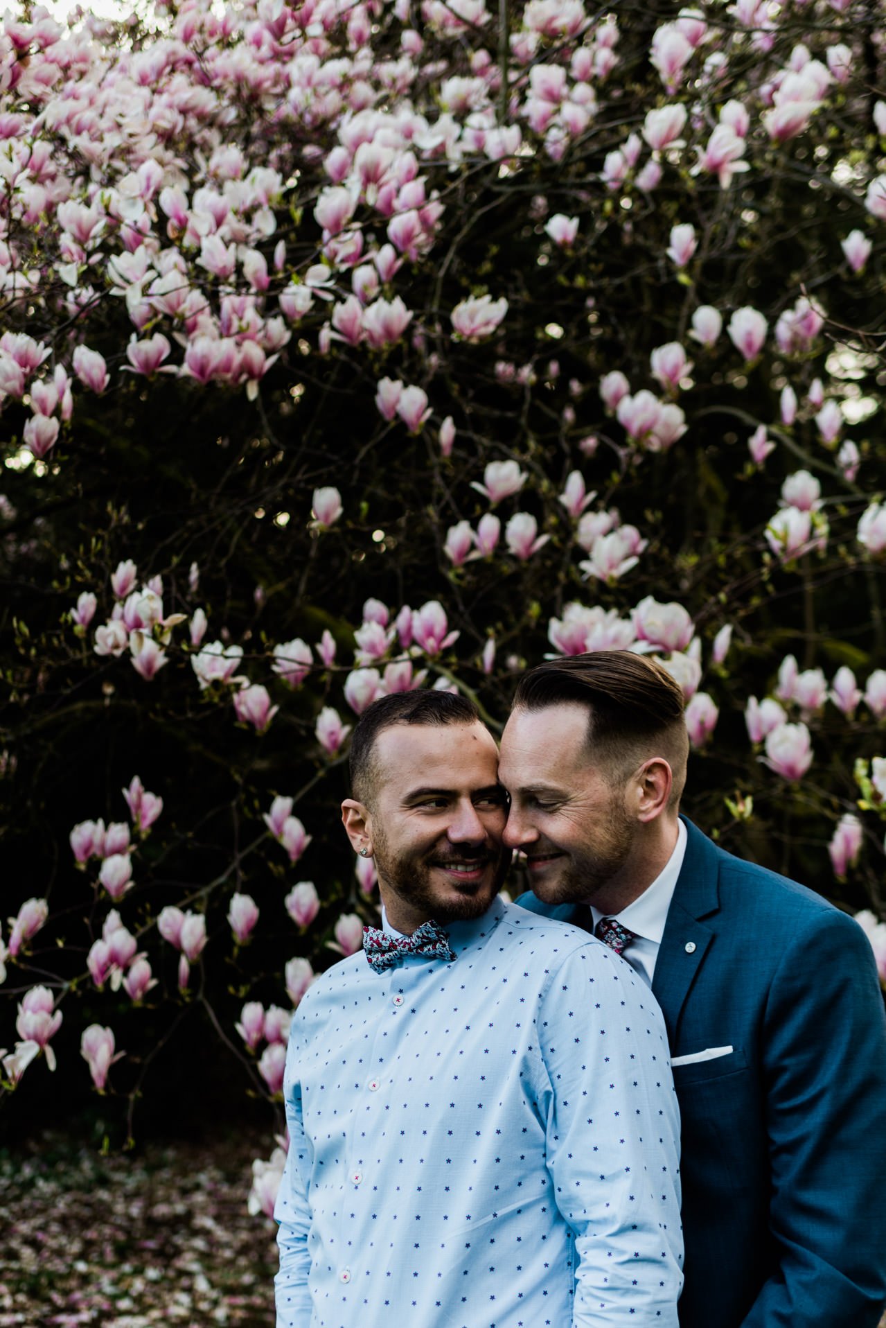 Gay couple poses in front of magnolia tree for Spring engagement session.
